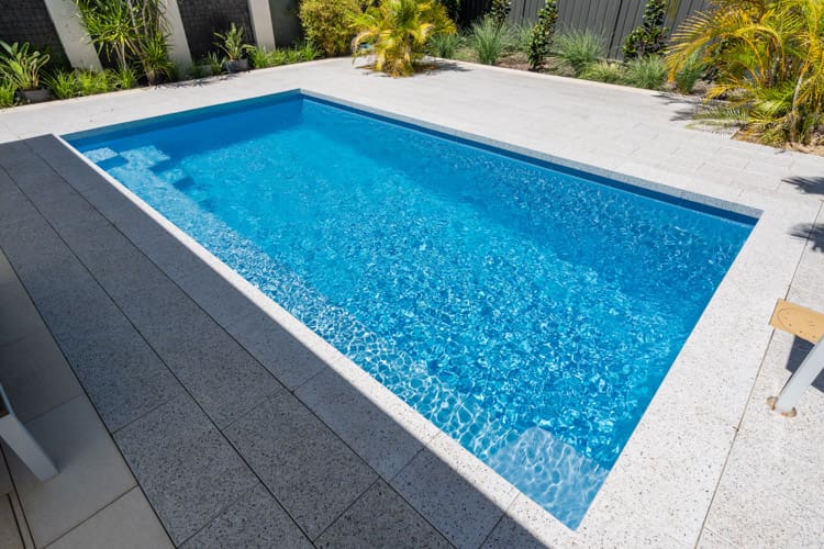 Clear blue swimming pool surrounded by paving
